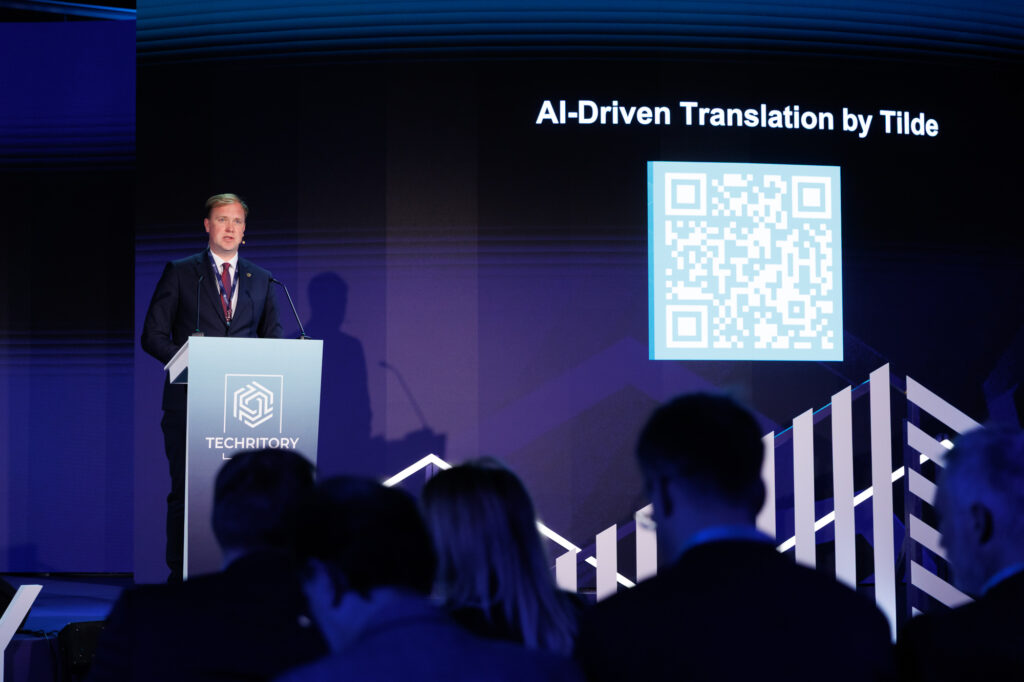 Runātājs ar QR kodu aiz viņa, kas noved pie Tilde Event Assistant risinājuma.